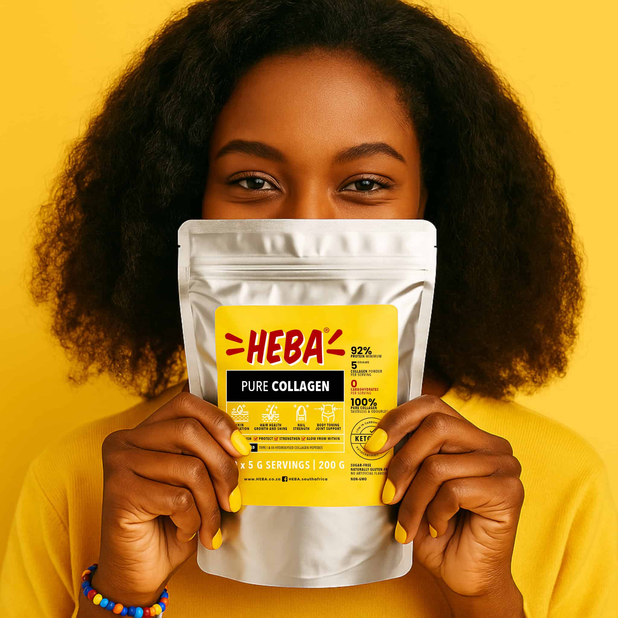 heba-pure-collagen-south-african-woman-hair-skin-nail-support Smiling South African woman holding a silver pouch of HEBA Pure Collagen in front of her face, wearing yellow nail polish and beaded bracelet, promoting healthy hair growth, skin hydration, and nail strength on a bright yellow background.